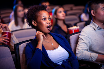African American woman in shock watching a movie in cinema.
