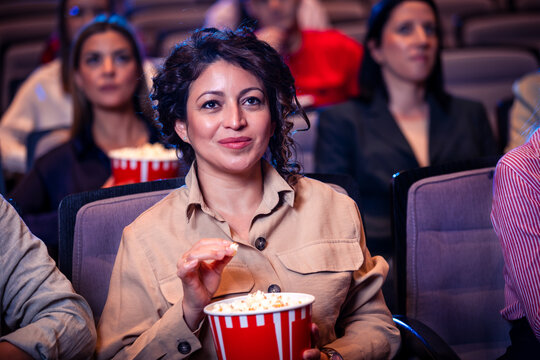 Hispanic woman watchin movie in cinema and eating popcorn.