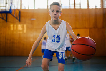 A junior basketball player in action dribbling a ball at indoor court.