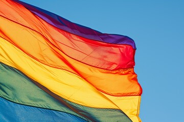 Bold and colorful pride flag waves gracefully against a clear blue sky, symbolizing lgbtq+ rights, inclusivity, and diversity with its vivid hues reflecting the joyful spirit of freedom and equality