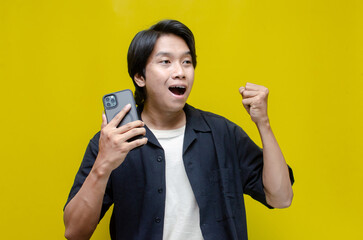 a funny young Asian man holding phone and dancing happily. asian man with joyful expression holding...