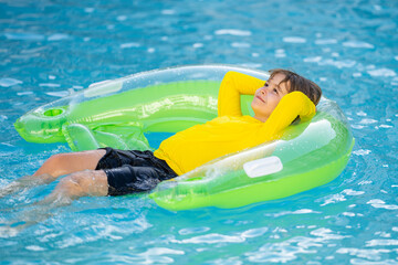 Happy young child enjoying summer vacation outdoors in water in the swimming pool. Cute little kid in swimming suit swim on an inflatable ring. Kid floating in a pool.