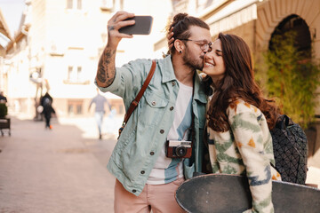 Romantic alternative couple taking selfies and kissing on a city street