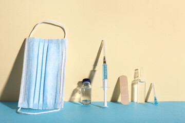 Medical syringe with medicine, mask and ampoules on color background