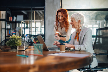 An old and young businesswomen smiling at laptop at the office.
