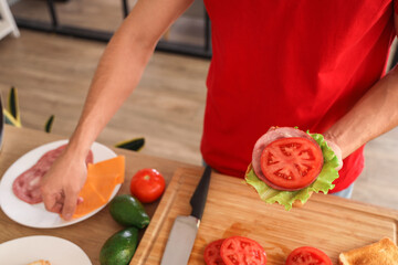 Young man making delicious sandwich with crispy toasts in kitchen, closeup
