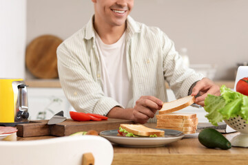 Young man preparing ingredients for tasty sandwich in kitchen