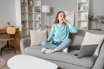 Young woman yawning on grey couch in living room