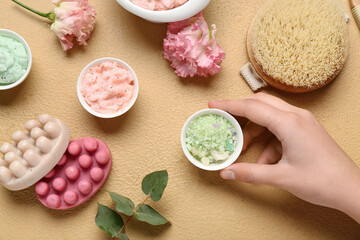 Female hand with different body scrubs and bath supplies on color background, closeup