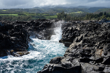 Rocky island landscape of blue Pacific Ocean waves crashing on lava rock, as a nature background

