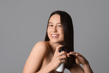 Young woman with cosmetics for hair treatment on grey background