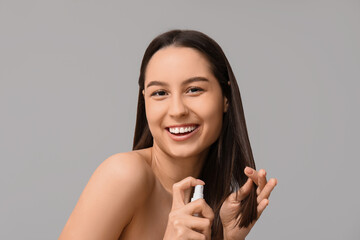 Young woman with cosmetics for hair treatment on grey background