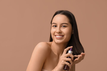 Young woman with cosmetics for hair treatment on beige background