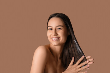 Young woman using cosmetics for hair treatment on beige background