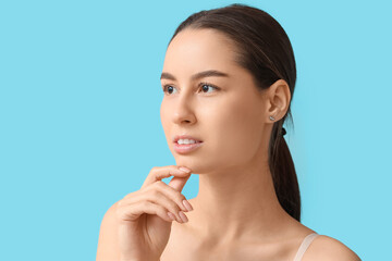 Young woman with hand near her face on blue background. Nose plastic surgery concept