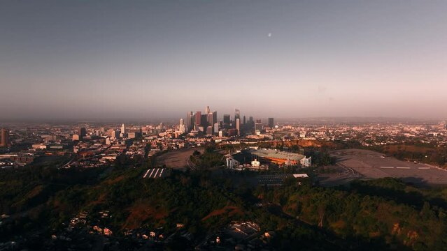 Aerial view of Dodger stadium and skyscrapers in downtown Los Angeles during sunrise with moon in the clear sky