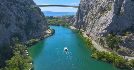 AERIAL: Leisure boat cruises along a verdant river gorge with high rocky cliffs.