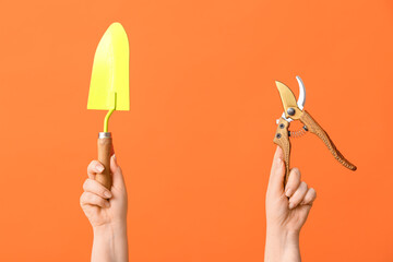 Female hands with gardening shovel and secateurs on color background, closeup