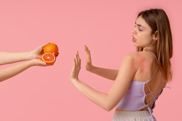 Young woman with skin allergy and female hands with grapefruit on pink background