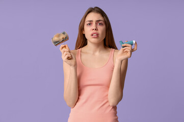 Young woman with dirty pet brush and inhaler suffering from allergy on purple background