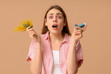 Young woman with mimosa and inhaler suffering from allergy on brown background