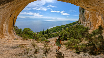 Young lady hiking with her dog through scenic mountain hollow with amazing view of coast and Adriatic Sea. Incredible views while exploring picturesque natural attractions on sunny island of Hvar. © helivideo