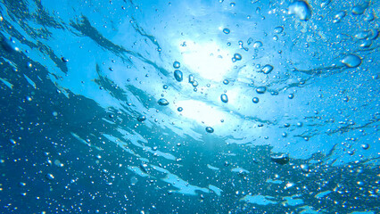 UNDERWATER: Crystal clear blue water with bubbles rising towards the sunlight. The shimmering light...