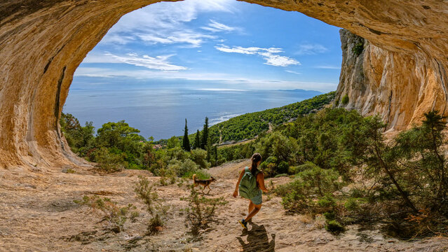 Young lady hiking with her dog through scenic mountain hollow with amazing view of coast and Adriatic Sea. Incredible views while exploring picturesque natural attractions on sunny island of Hvar.