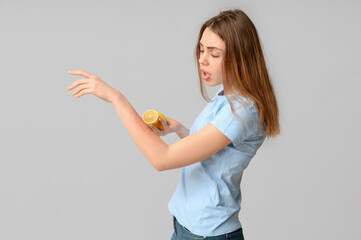 Young woman with skin allergy and lemon on grey background