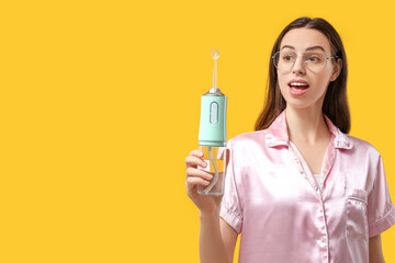 Beautiful young woman with oral irrigator on yellow background