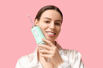 Beautiful young woman with oral irrigator on pink background