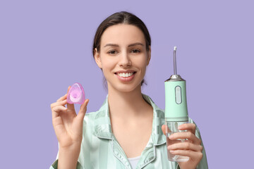 Beautiful young woman with oral irrigator and dental floss on lilac background