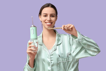 Beautiful young woman with oral irrigator and toothbrush on lilac background