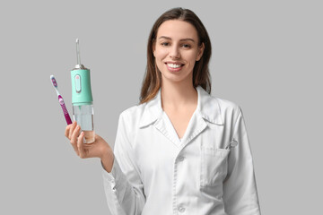 Female dentist with oral irrigator and toothbrush on grey background