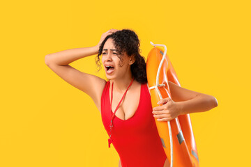 Beautiful young shocked African-American female lifeguard with ring buoy screaming on yellow...