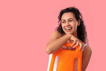 Beautiful young happy African-American female lifeguard with rescue buoy on pink background