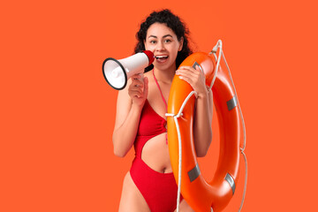 Beautiful young happy African-American female lifeguard with ring buoy and megaphone on orange...