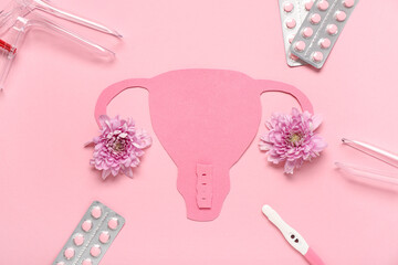 Paper uterus with gynecological speculums, pills, pregnancy test and chrysanthemum flowers on pink background