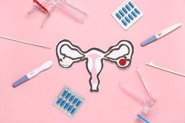 Paper uterus with gynecological speculums, pills and pap smear test tools on pink background