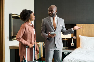 Portrait of luxury hotel manager welcoming young Black woman entering hotel room enjoying travel...
