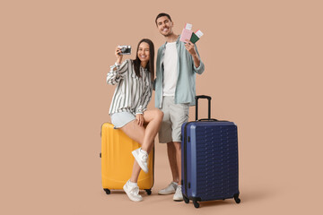 Beautiful young happy couple of tourists with suitcases, passports and camera on brown background