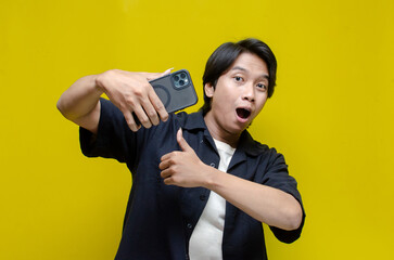 a funny young Asian man holding phone and dancing happily. asian man with joyful expression holding...