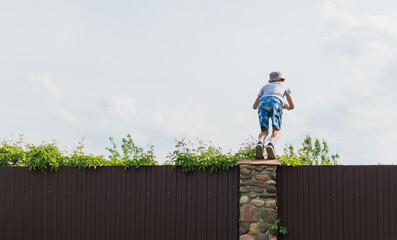 A little boy climbs over a fence on a private plot