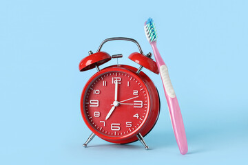 Red alarm clock and toothbrush on blue background