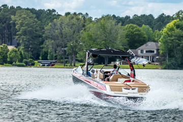 Boaters on red wakeboard wake boat enjoying summer day on freshwater lake.