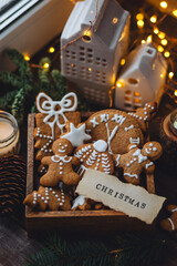 Handmade zero waste gift for Christmas or New Year. Wooden box with homemade delicious gingerbread cookies decorated with white icing. Cozy home atmosphere, fairy lights, fir tree branches