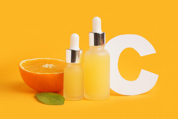 Bottles of essential oil, paper letter C and orange on color background