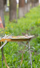 An artist's easel stands in a verdant field, equipped with a canvas, paintbrushes, and an array of...