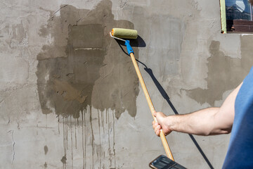 A man applies primer to a concrete wall using a roller. The image shows the process of painting...