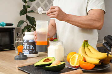 Sporty muscular man pouring protein powder into bottle for shake in kitchen, closeup